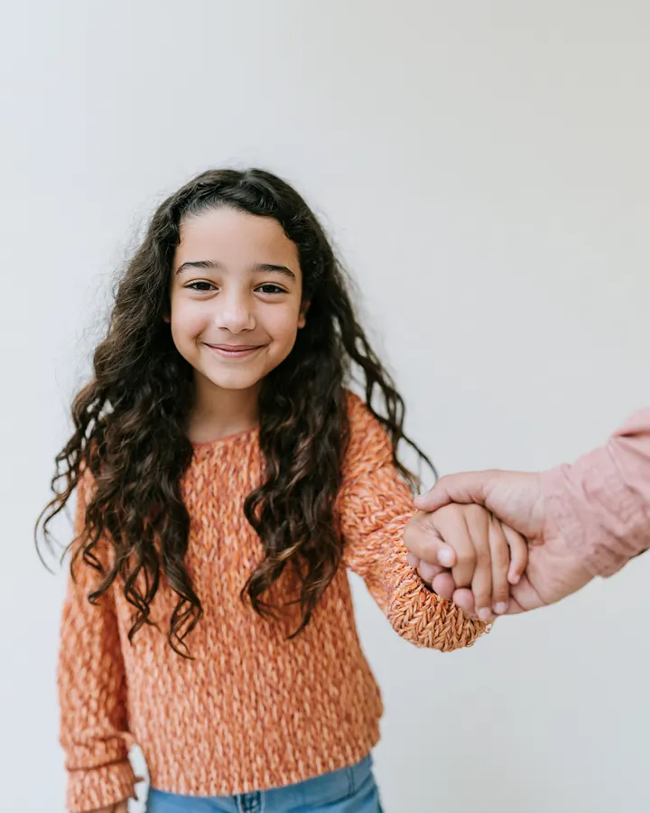 Menina de cabelo comprido sorrindo, de mão dada com um adulto